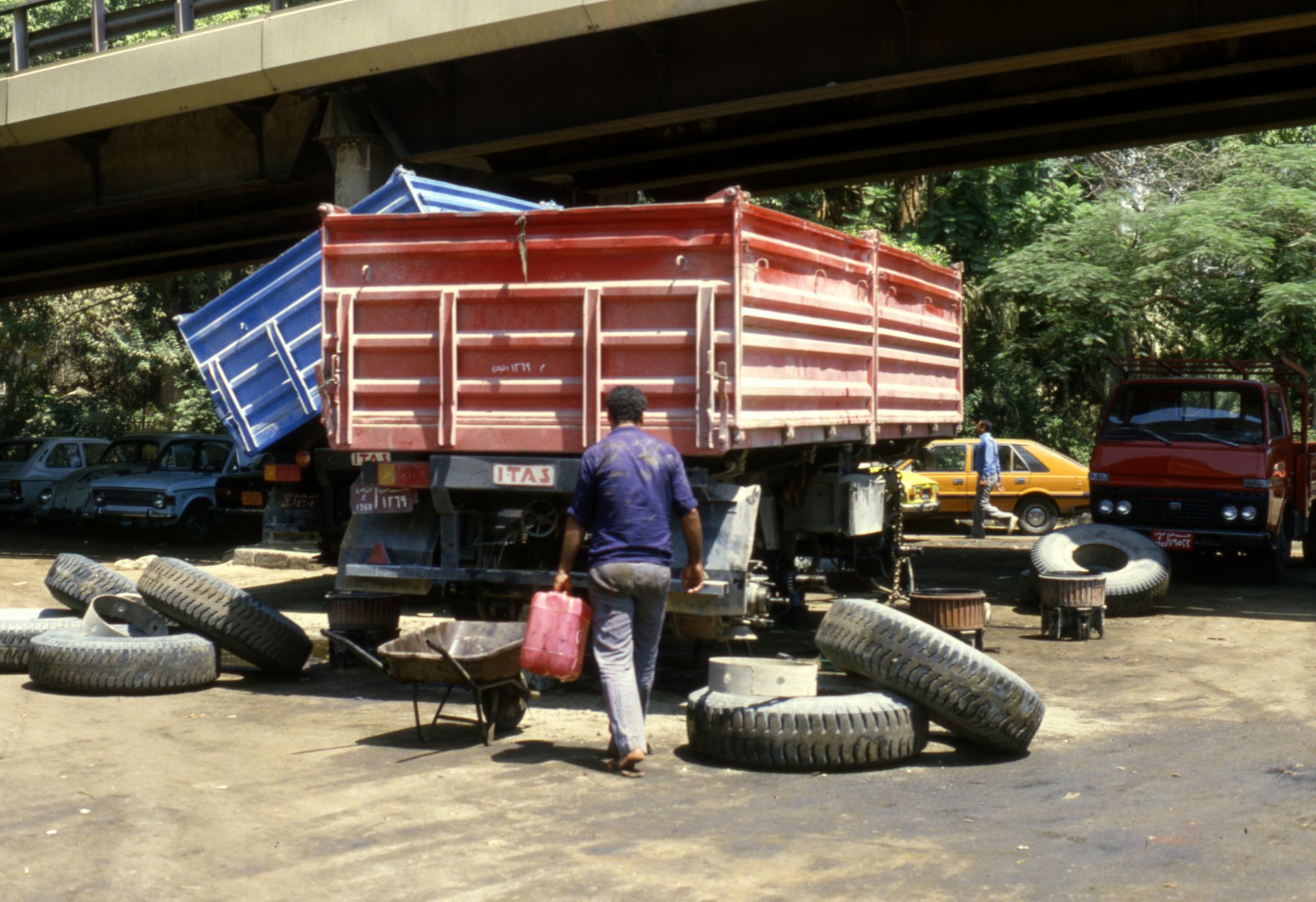 man in blue polo shirt and blue denim jeans standing near red truck during daytime